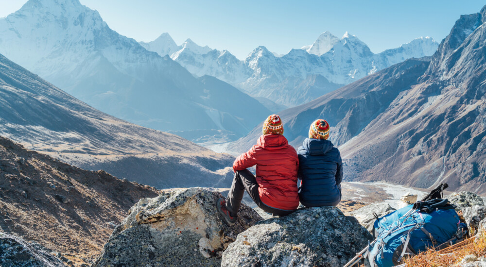 Couple resting on the Everest Base Camp trekking route near Dughla 4620m. Backpackers left Backpacks and trekking poles and enjoying valley view with Ama Dablam 6812m peak and Tobuche 6495m
