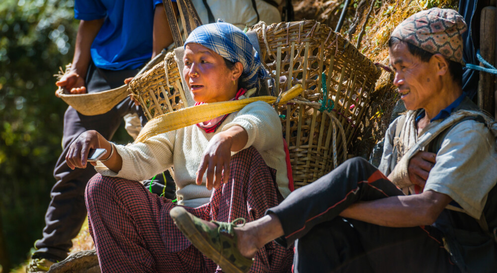 Porters resting whilst carrying heavy loads using a traditional doko bamboo basket and namlo head band on the Everest base camp trail deep in the Himalayan mountains of Nepal.